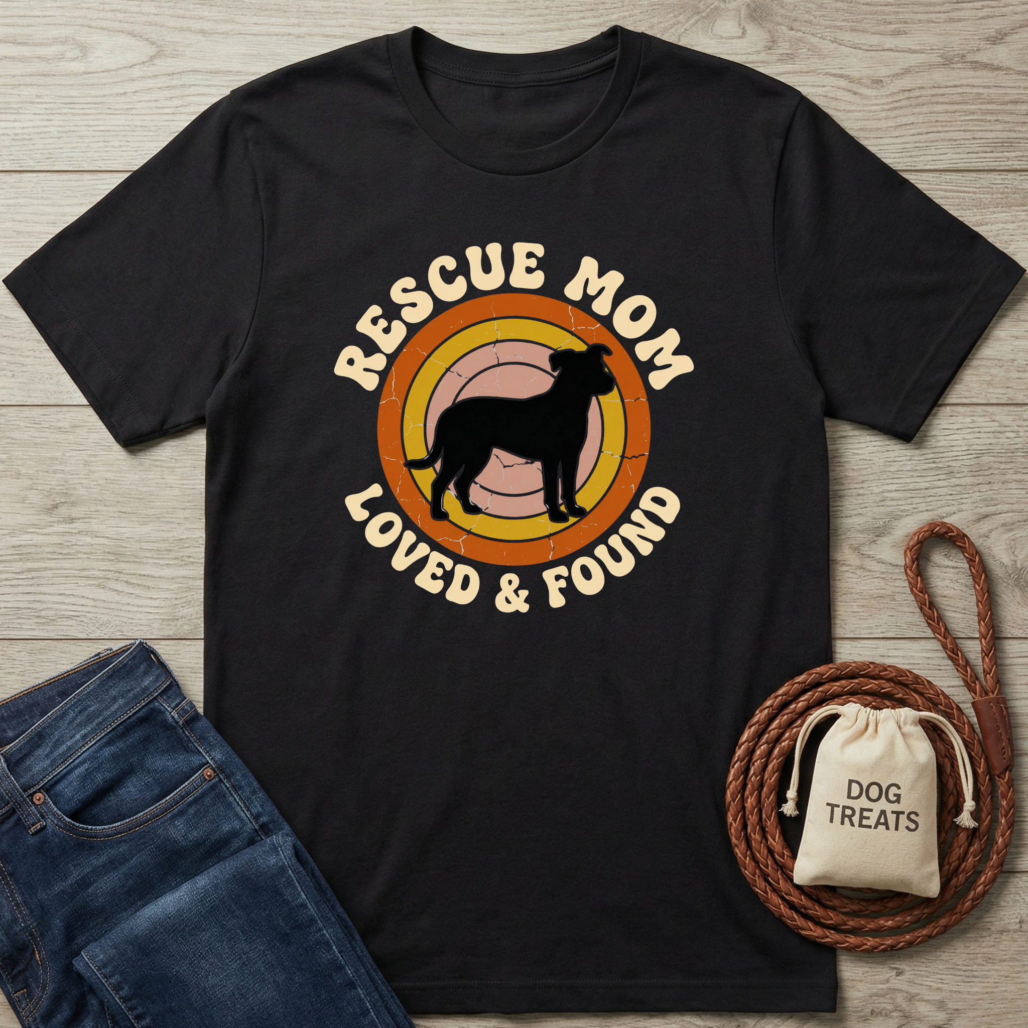 Black t-shirt with 'Rescue Mom Loved & Found' design on a wooden surface with jeans and a dog treat bag.