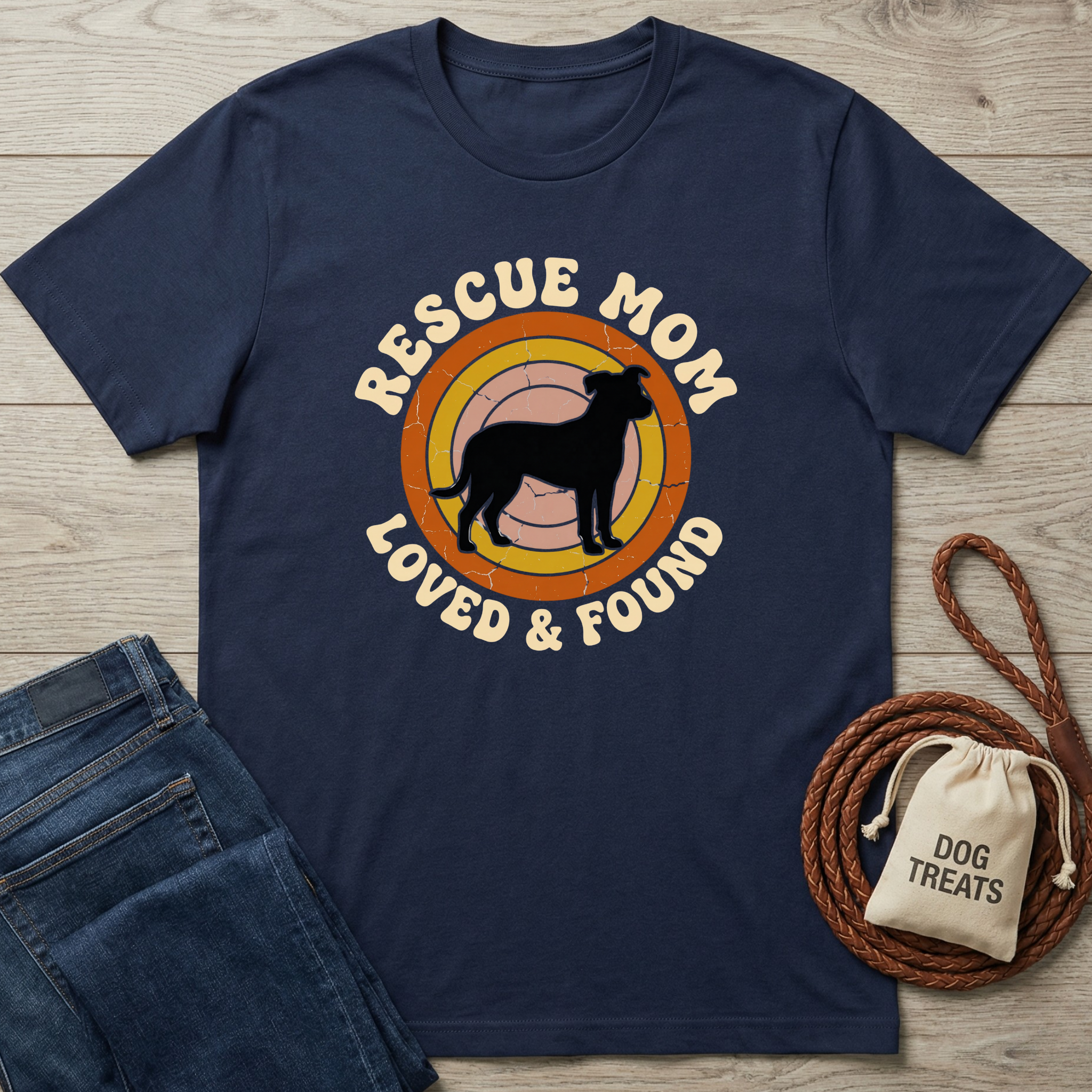 Navy blue t-shirt with 'Rescue Mom Loved & Found' graphic on a wooden surface with jeans and a dog treat bag.