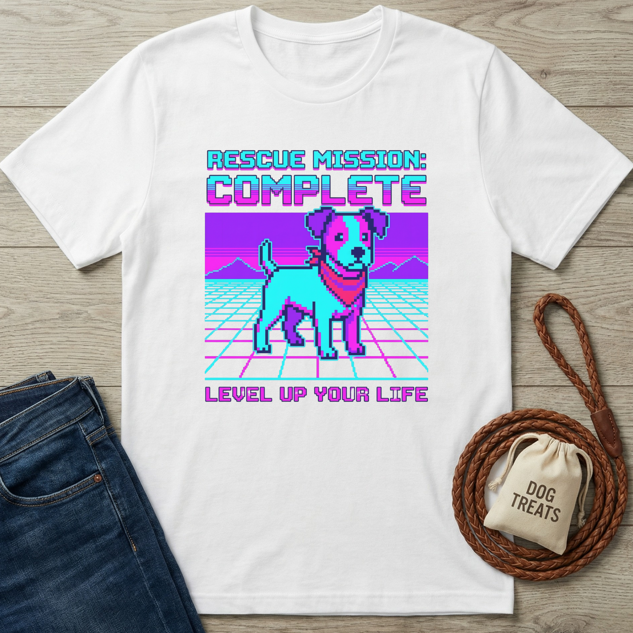 White t-shirt with a dog graphic and text on a wooden surface with jeans and a dog treat bag.