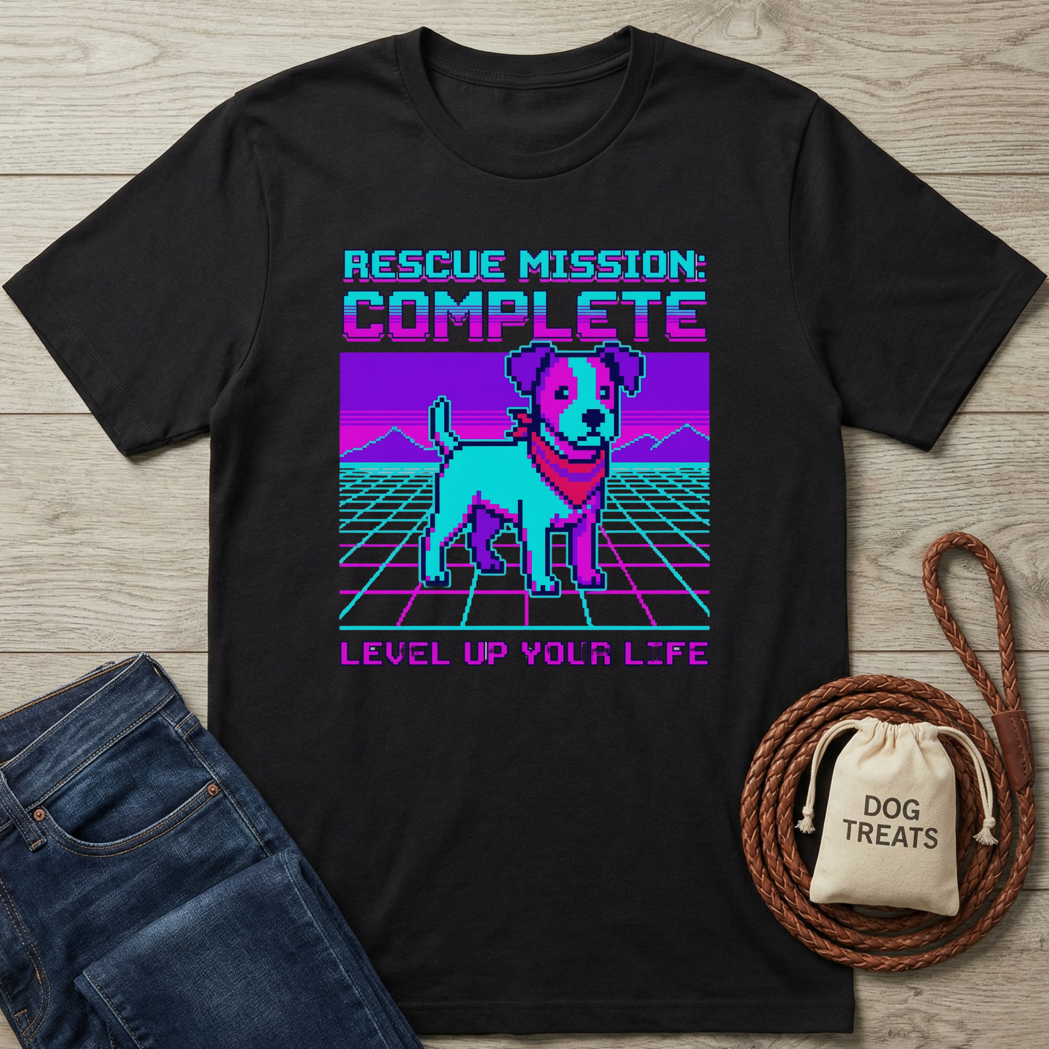 Black t-shirt with a graphic of a dog and text 'Rescue Mission: Complete, Level Up Your Life' on a wooden surface with jeans and a bag of dog treats.