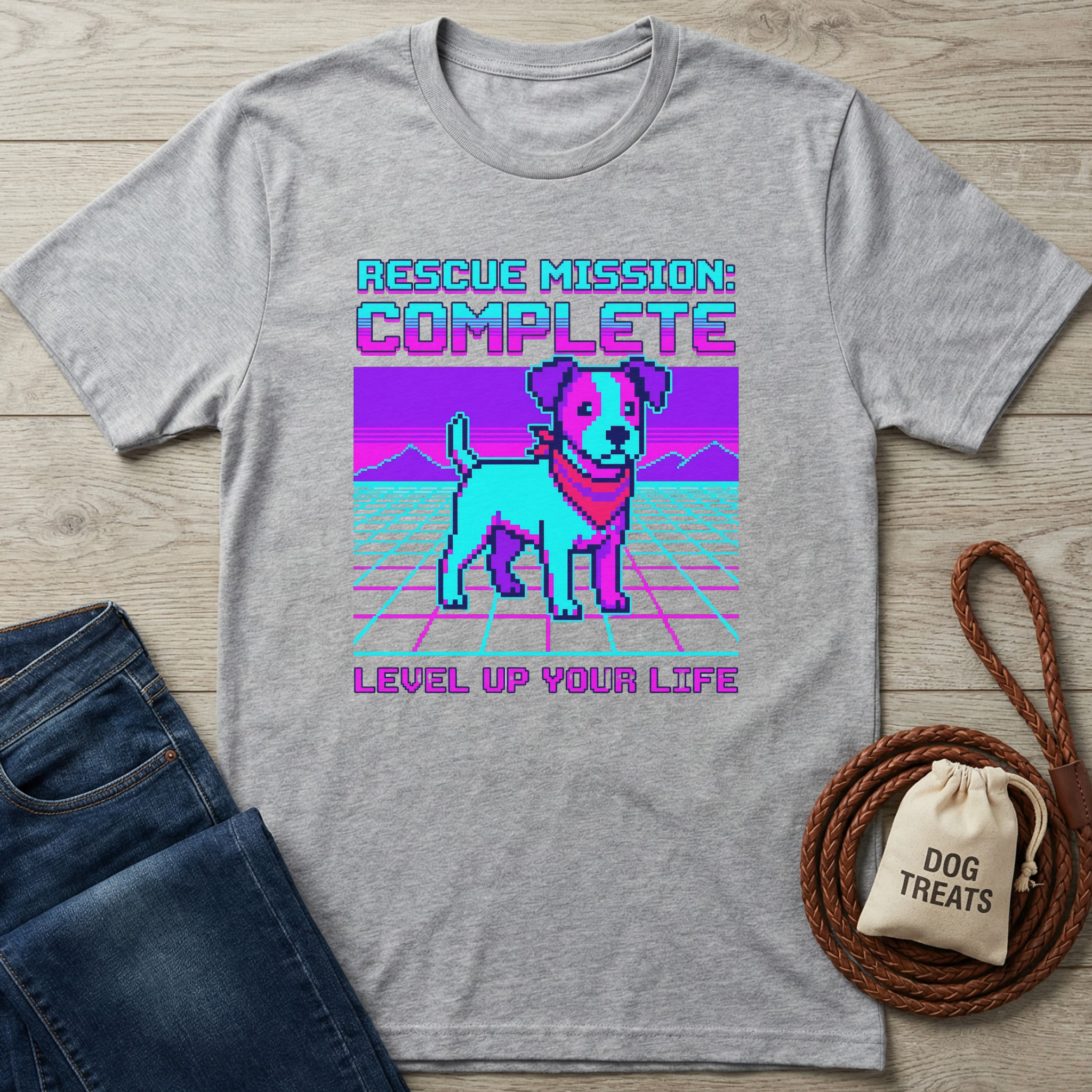 Gray t-shirt with a dog graphic and text on a wooden surface with jeans and a dog treat bag.