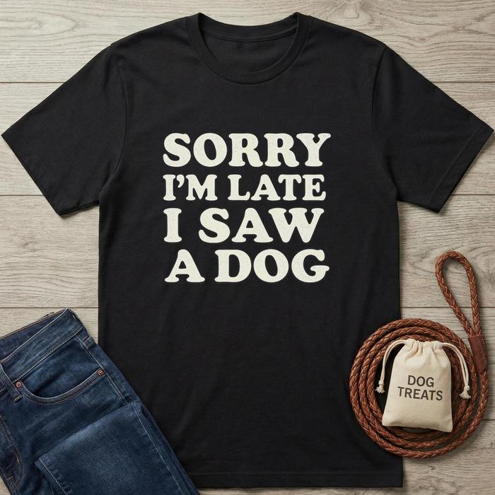 Black cotton t-shirt with "SORRY I'M LATE I SAW A DOG" in cream text, next to jeans and dog treats.