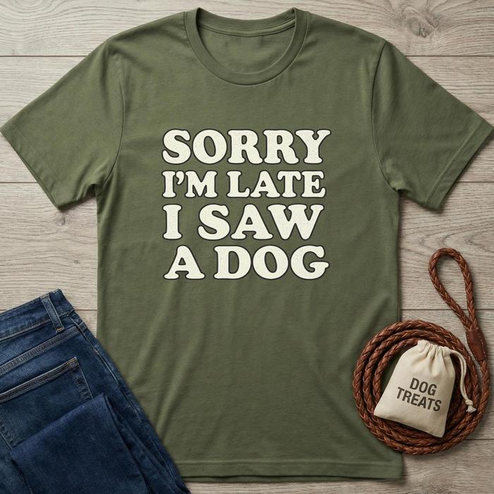 Olive green t-shirt with "SORRY I'M LATE I SAW A DOG" in white text, next to jeans and dog treats.