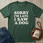Dark green cotton t-shirt with "SORRY I'M LATE I SAW A DOG" text, next to jeans and dog leash.