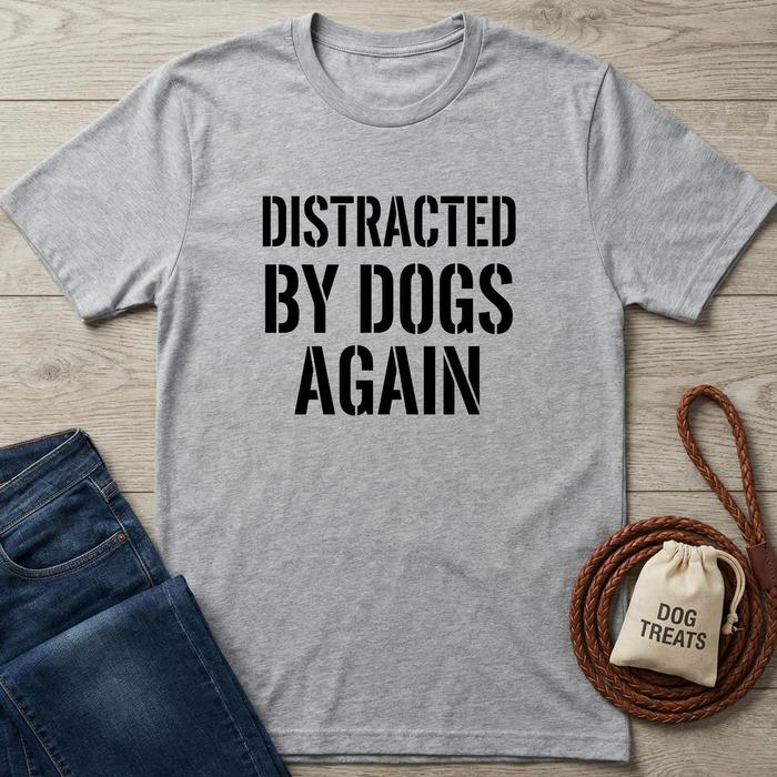 Gray t-shirt with 'Distracted by Dogs Again' text on a wooden surface with dog accessories.