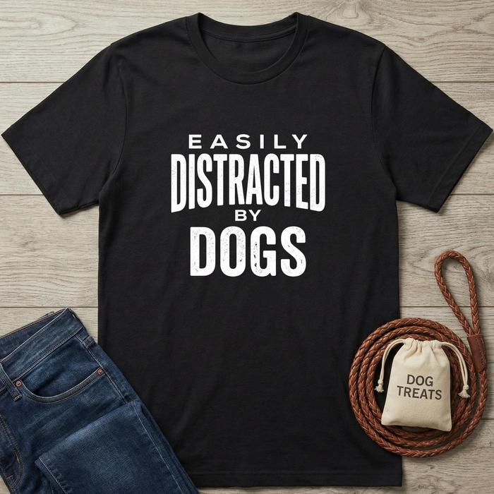Black t-shirt with 'Easily Distracted by Dogs' text, next to jeans and a dog treat bag on a wooden surface.