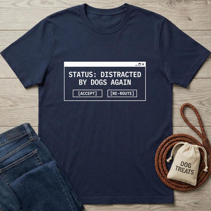 Navy blue t-shirt with 'Status: Distracted by Dogs Again' text on a wooden surface with jeans and a dog treat bag.