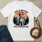 White t-shirt with a graphic of a dog and text 'Life is better with a rescue dog' on a wooden surface with accessories.