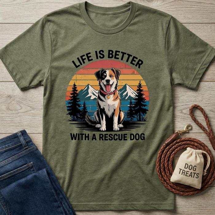 Green t-shirt with a dog graphic and text 'Life is better with a rescue dog' on a wooden surface, with jeans and a dog treat bag.