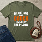 Green t-shirt with humorous text on a wooden surface with jeans and a dog treat bag.
