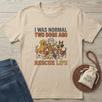 Beige cotton t-shirt with "I WAS NORMAL TWO DOGS AGO RESCUE LIFE" text and cartoon dogs.