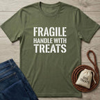 Olive green cotton t-shirt with "FRAGILE HANDLE WITH TREATS" in white text, next to jeans and dog treats bag.