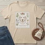 Beige cotton t-shirt with a detailed golden retriever and botanical flower design, next to jeans and a dog treat bag.