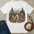 White cotton t-shirt featuring a Basset Hound resting on a trail with mountains, hiking boots, and a backpack graphic.
