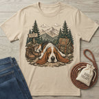 Beige crewneck t-shirt featuring a Basset Hound resting on a trail with mountains, hiking boots, and a backpack graphic.