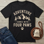 Black cotton t-shirt with "Adventure Comes With Four Paws" mountain graphic, next to jeans and dog treats.