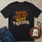 Black cotton t-shirt with "Dogs Are My Best Friends" in orange and yellow retro font, next to jeans and dog treats.