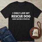 Black Gildan Softstyle® 64000 tee with "I ONLY LIKE MY RESCUE DOG" text, next to jeans and dog accessories.