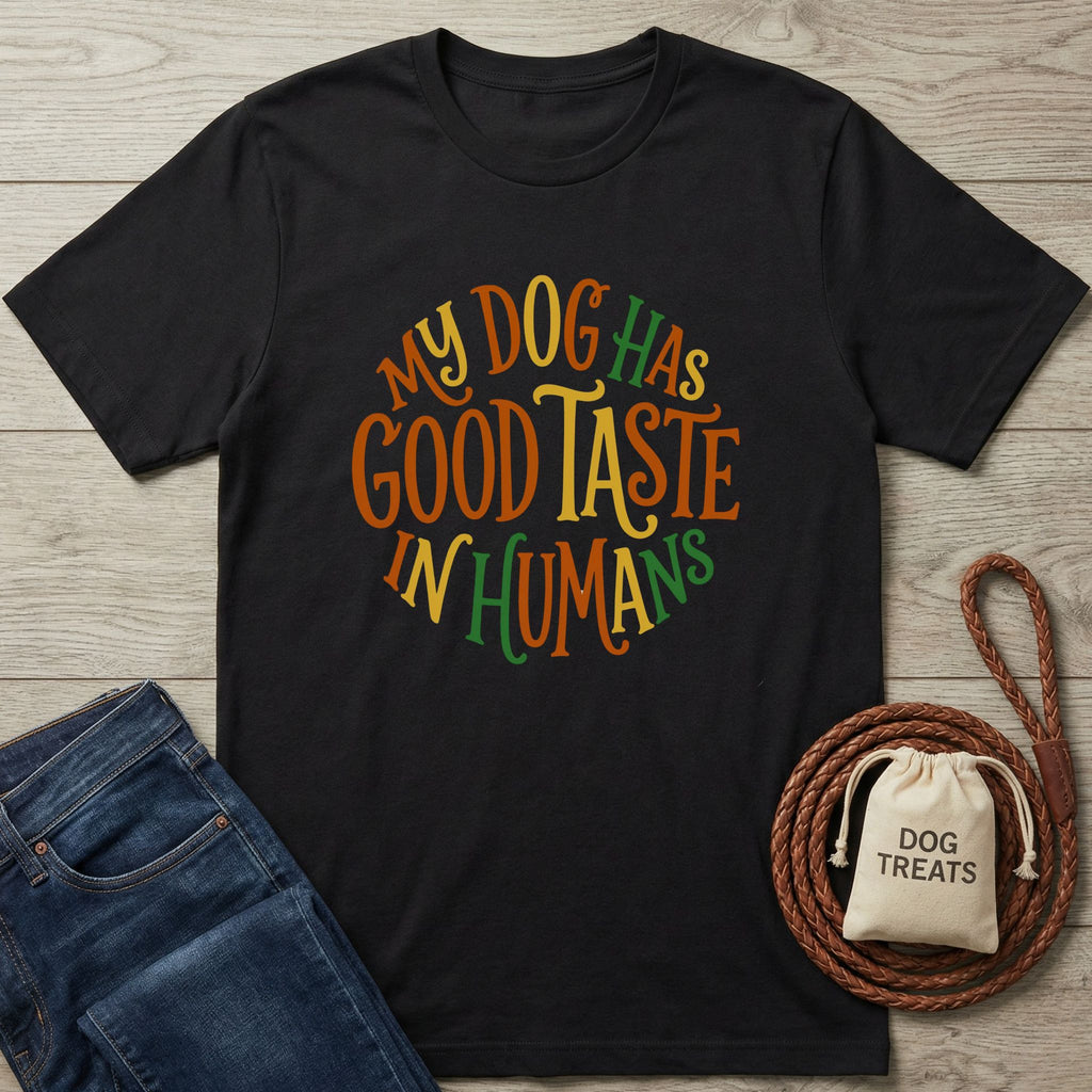 Black Gildan Softstyle t-shirt with "My Dog Has Good Taste In Humans" in colorful, playful text.