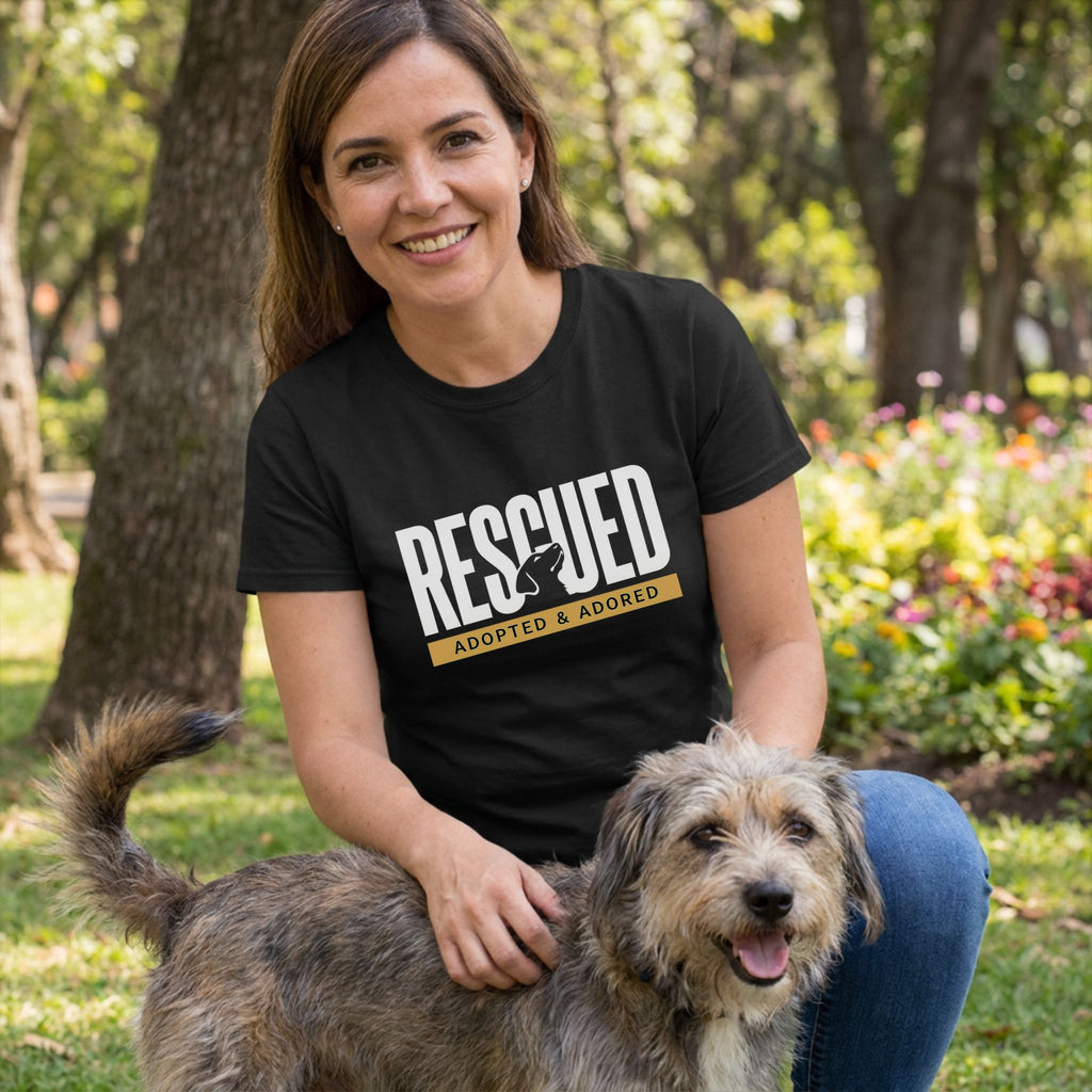 Woman in a black "RESCUED ADOPTED & ADORED" tee petting a scruffy dog in a park.