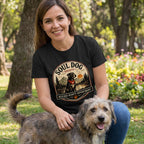 Woman in black "Soul Dog Society" t-shirt with a graphic of a black dog by a lake at sunset, petting a scruffy dog.
