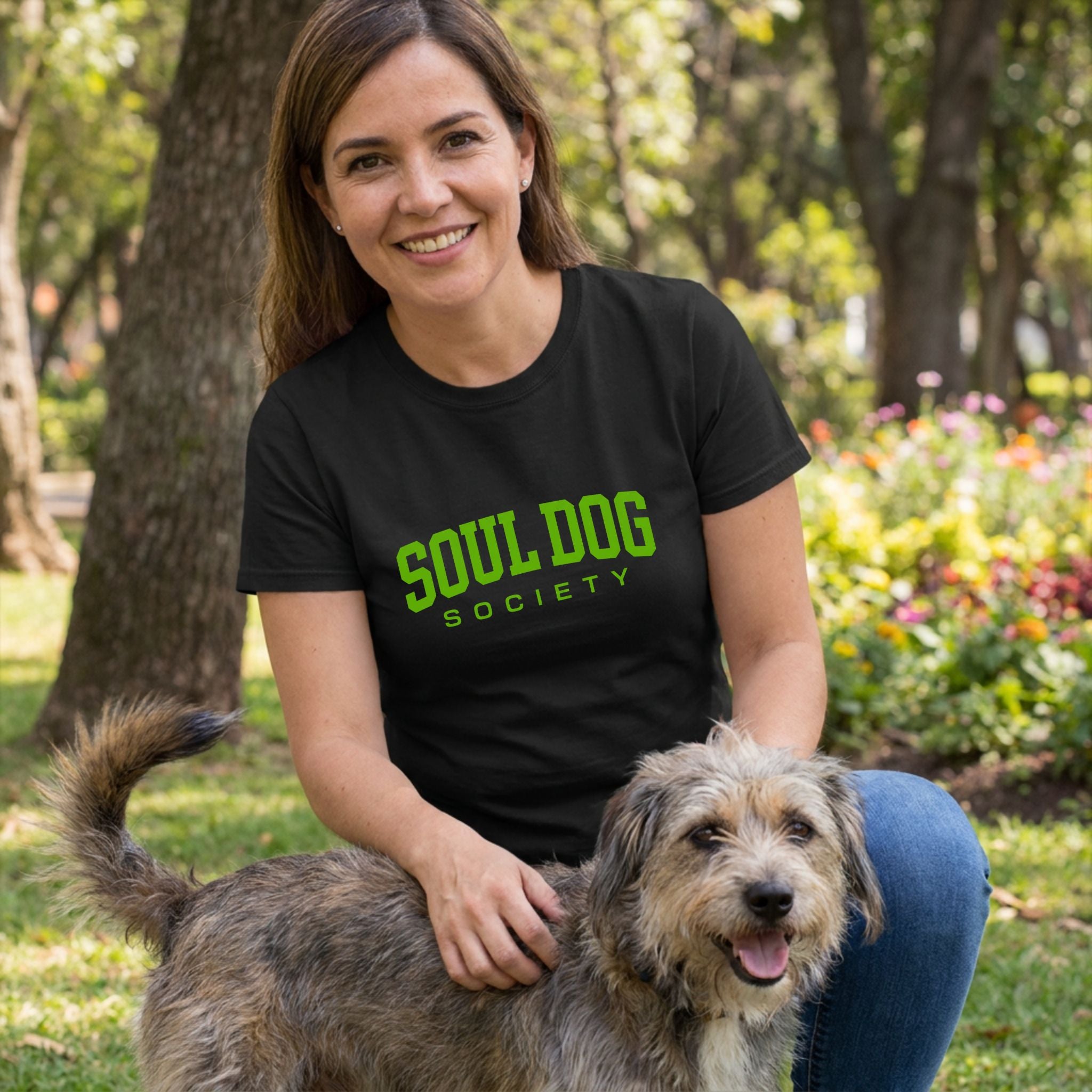 Woman in a black Soul Dog Society t-shirt with green text, petting a rescue dog outdoors.