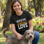 Woman in a black "Rescue Dog = Unconditional Love" t-shirt petting a scruffy dog in a park.