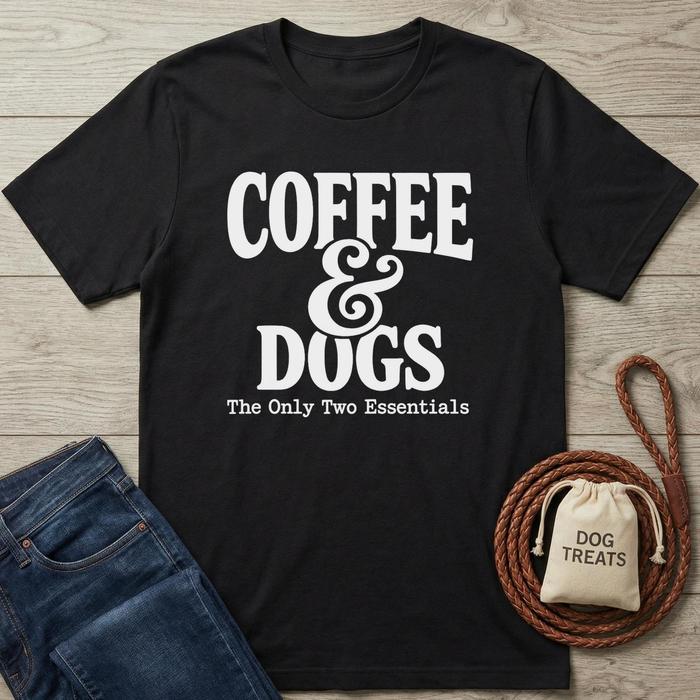 Black crewneck t-shirt with "Coffee & Dogs: The Only Two Essentials" in white text, next to jeans and dog treats.