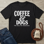 Black crewneck t-shirt with "Coffee & Dogs: The Only Two Essentials" in white text, next to jeans and dog treats.