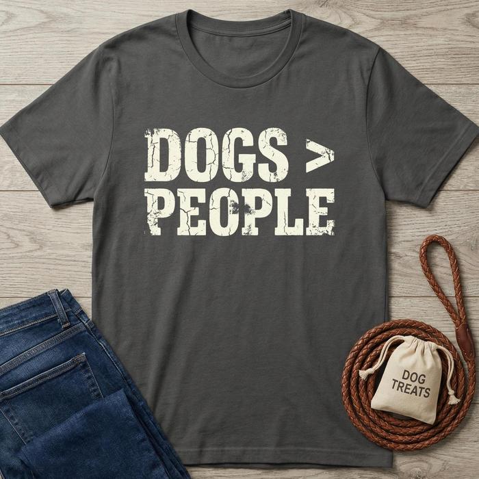 Charcoal gray "Dogs > People" distressed print t-shirt, folded beside blue jeans and a treat bag on wood.
