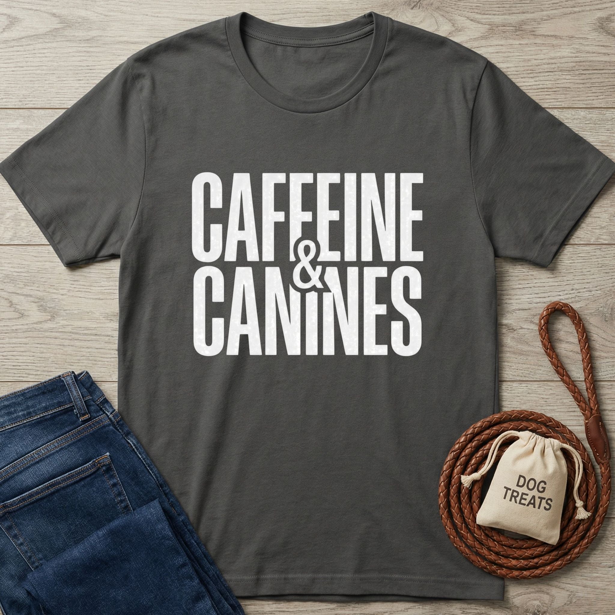 Dark gray Gildan Softstyle® t-shirt with "CAFFEINE & CANINES" in white text, next to jeans and dog treats.