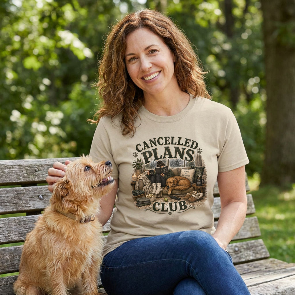 Woman wearing a beige crewneck T-shirt with a Cancelled Plans Club graphic, sitting on a bench with a small dog.