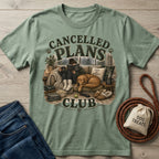 Sage green crewneck t-shirt featuring a cozy graphic of a person reading with a dog on a couch, with Cancelled Plans Club text.