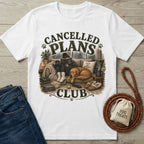 White cotton t-shirt featuring a cozy illustration of a person reading with a dog on a couch, labeled Cancelled Plans Club.