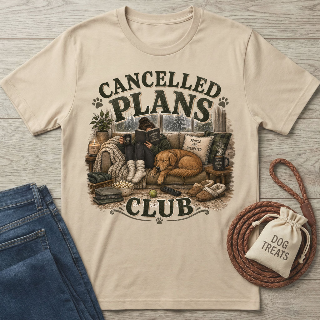 Beige crewneck t-shirt featuring a graphic of a person reading on a couch with a dog, coffee, and cozy home decor.