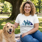 Woman in white "Canine Explorer" tee with geometric dog and mountains, petting a golden retriever in a park.