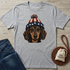 Gray t-shirt with a dachshund wearing a red, white, and blue stars and stripes pom-pom hat.