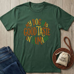 Forest green Gildan Softstyle® t-shirt with "My Dog Has Good Taste In Humans" text, next to jeans and dog treats.