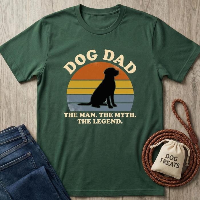 Forest green "Dog Dad" t-shirt with a black dog silhouette against a retro sunset, next to jeans and dog treats.