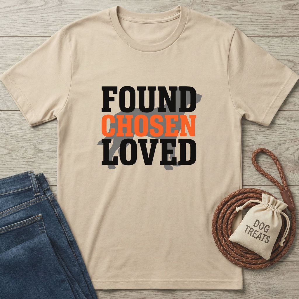 Beige Gildan Softstyle® t-shirt with "FOUND CHOSEN LOVED" text and a dog silhouette, next to jeans and dog treats.