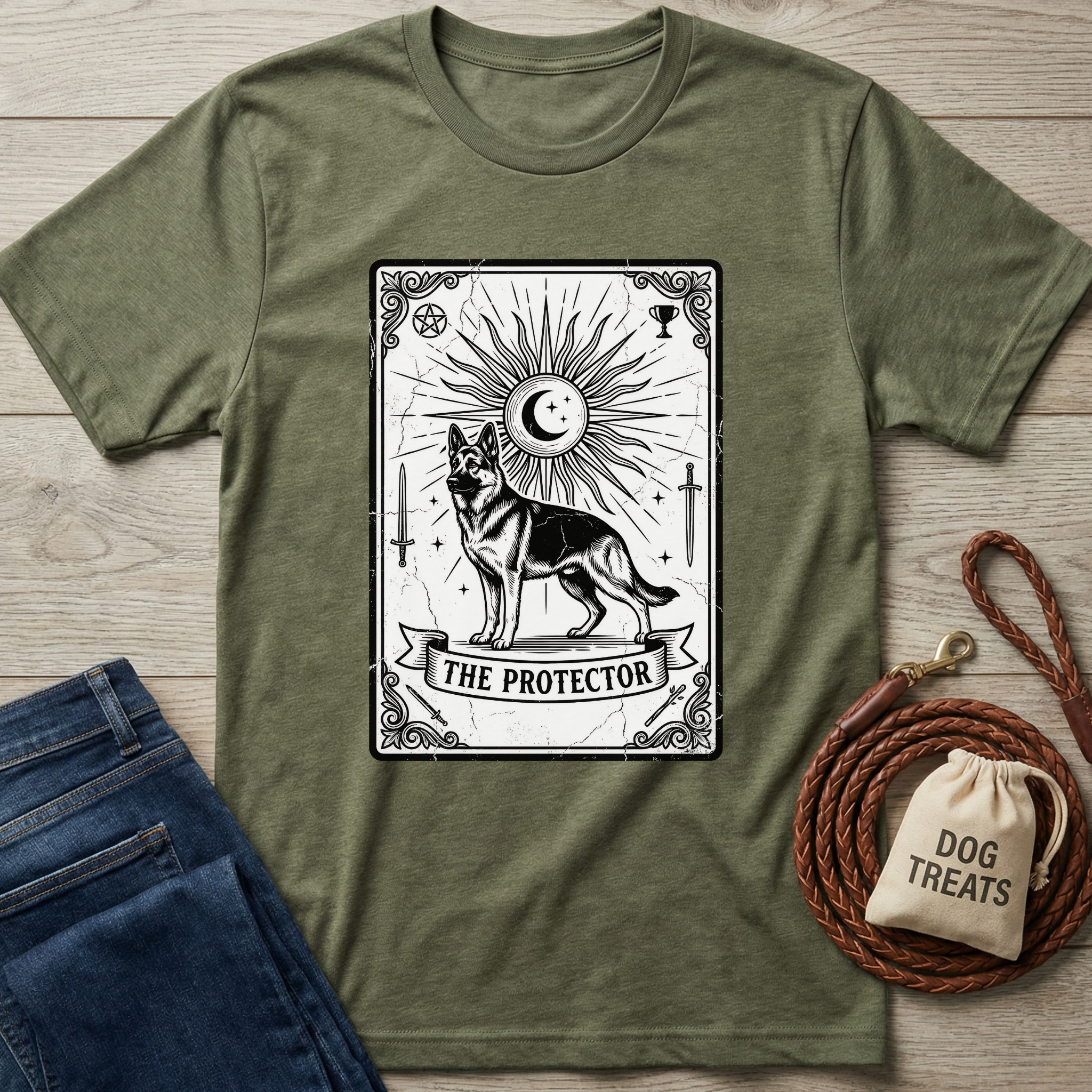Olive green "The Protector" Tarot card T-shirt with a German Shepherd design, next to jeans and dog treats.