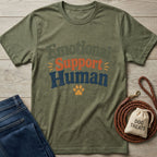 Olive green "Emotional Support Human" t-shirt with orange and blue text, a paw print, jeans, and dog treats.