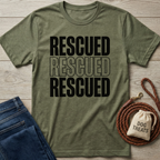 Olive green "Rescued" t-shirt with black text, next to blue jeans, a braided leash, and a "Dog Treats" bag.