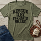 Olive green t-shirt with "Rescue Is My Favorite Breed" text, folded jeans, and a coiled leather leash with dog treats.