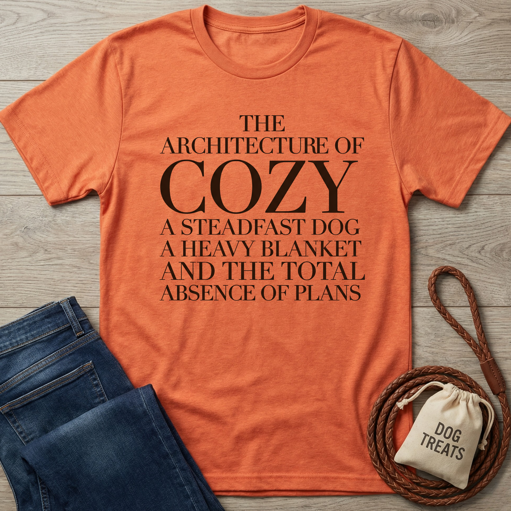 Orange crew-neck t-shirt with "The Architecture of Cozy" text, folded jeans, and dog treats bag.