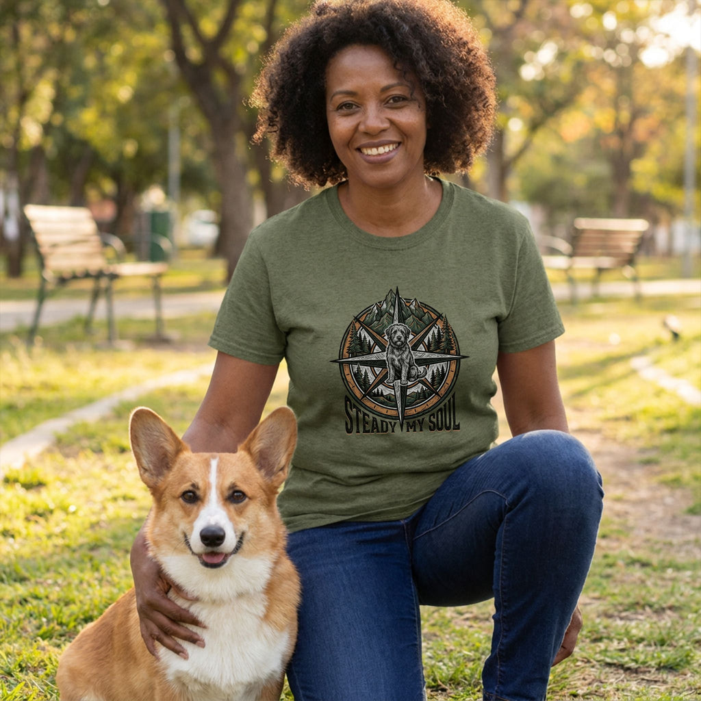 Woman in an olive green "Steady My Soul" t-shirt with a compass and dog design, kneeling with a Corgi.