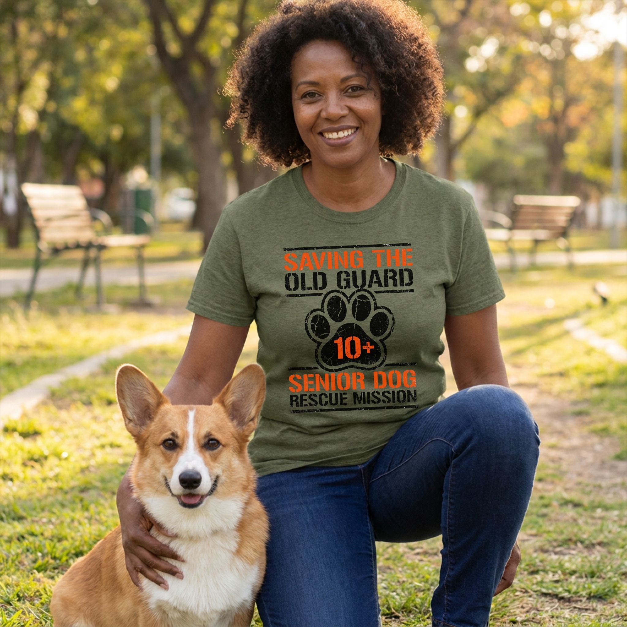 Woman in an olive green "Saving The Old Guard" senior dog rescue t-shirt, kneeling with a corgi.