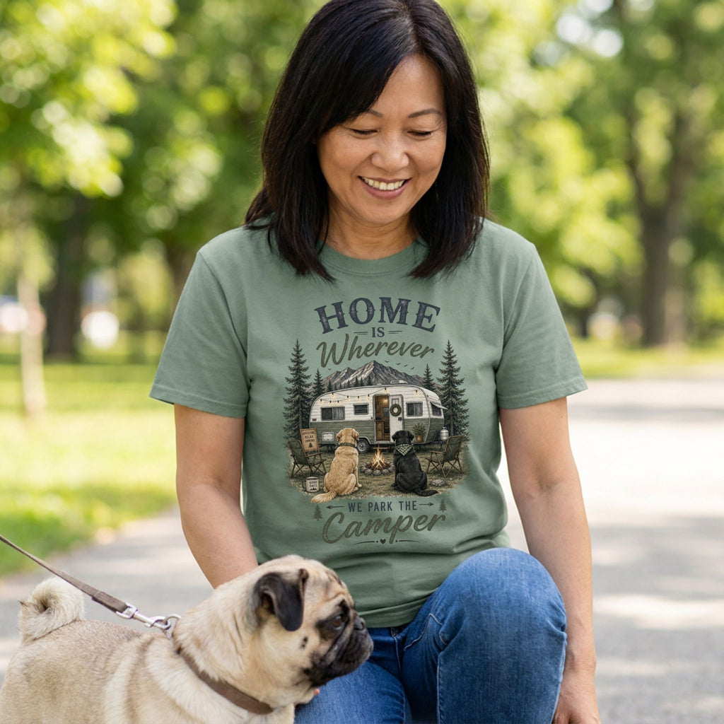 Woman wearing a sage green crewneck t-shirt featuring a camping-themed graphic of a vintage trailer, campfire, and two dogs.