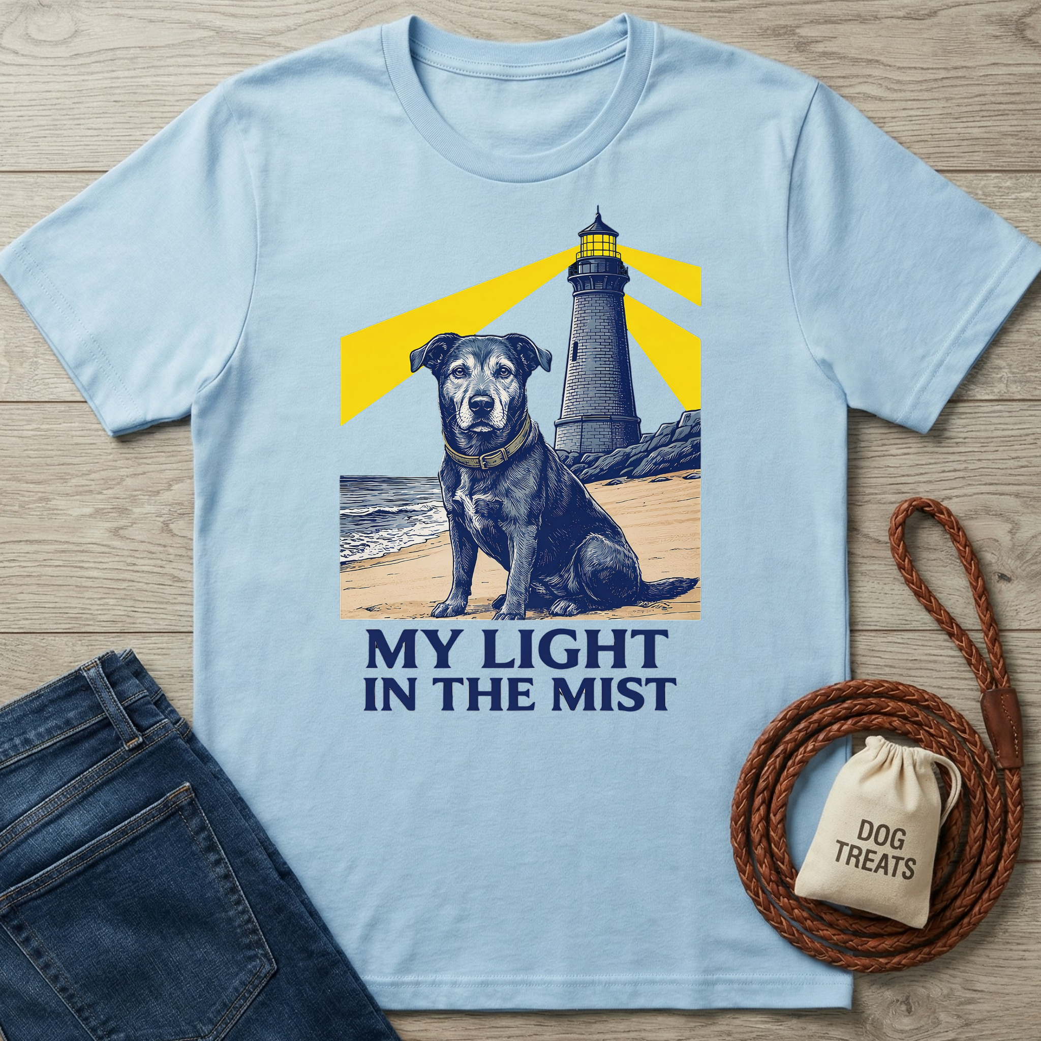 Light blue cotton t-shirt with a graphic of a black dog on a beach with a lighthouse and "MY LIGHT IN THE MIST" text.