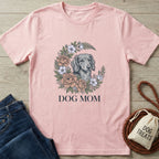 Pink Gildan Softstyle Dog Mom t-shirt with a floral wreath and dachshund graphic, next to jeans and dog treats.
